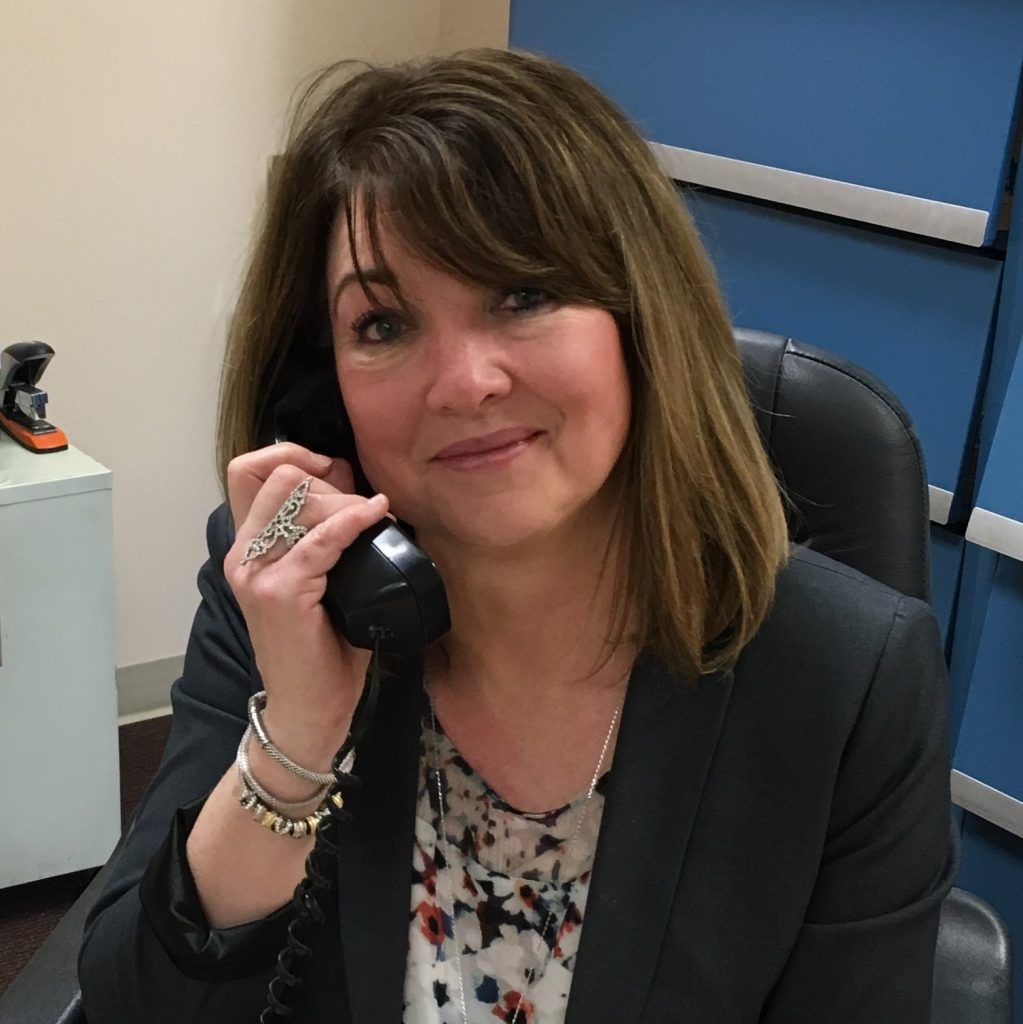 Miriam Miriam Roe-McDonald, office manager at Chicago Hearing Services, smiling while on the phone, in a professional setting with a filing cabinet in the background.