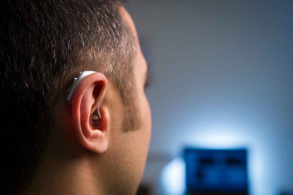 Man wearing a modern hearing aid, showcasing advancements in hearing technology, with a blurred background suggesting a digital environment.