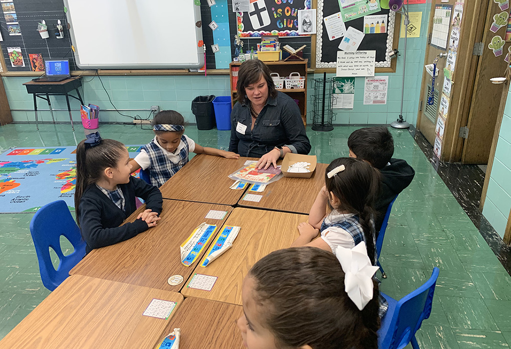 Children engaged in a learning activity with an instructor in a classroom, featuring educational materials on the table and a colorful map on the floor, highlighting community involvement in hearing health education.