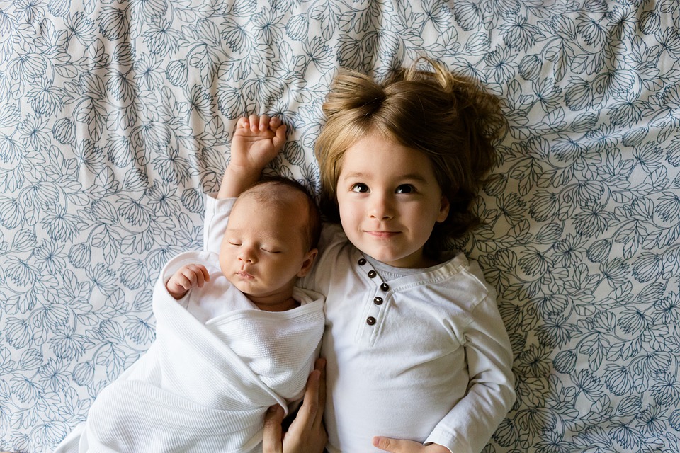 Child lying next to a sleeping baby on a floral-patterned blanket, emphasizing the importance of early hearing tests for children.