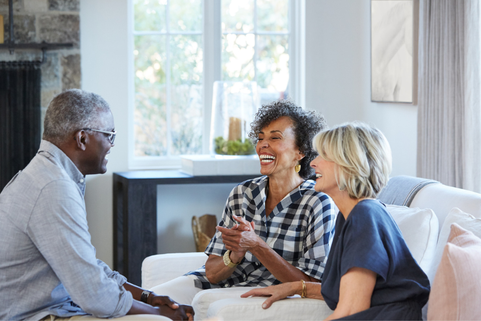 chicago-hearing-services-starting-the-conversation Three adults engaged in a friendly conversation in a cozy living room, emphasizing supportive dialogue about hearing loss and communication.