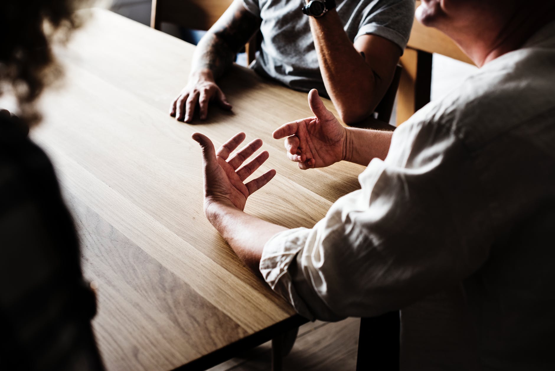 Hands gesturing during a discussion at a wooden table, representing communication and collaboration relevant to hearing health and audiology topics.